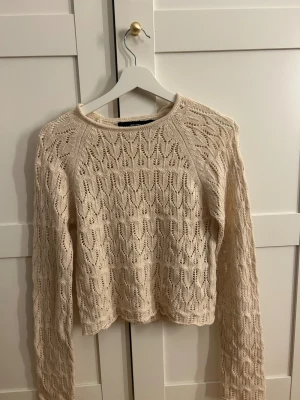 Beige stickad tröja från Vero Moda - Säljer en beige stickad tröja från Vero Moda i storlek S. Tröjan har ett snyggt hålmönster och är långärmad med rund hals. Perfekt för dig som gillar en chill och trendig look med lite boho-vibe.