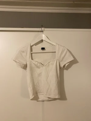 Vit ribbad topp från Gina Tricot - Vit ribbad topp från Gina Tricot i storlek S. orta ärmar, fyrkantig urringning med v-ringad detalj framtill
