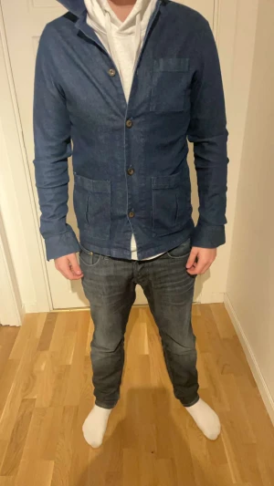 John henric overshirt  - Snygg mörkblå jeansjacka med klassisk krage och tre framfickor. Jackan har knäppning med bruna knappar och är långärmad. Materialet är jeans och passformen är normal. Perfekt för dig som gillar en stilren och enkel look.