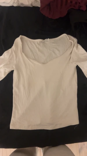 Ribbad vit topp med v-ringning - Säljer en ljus, ribbad topp i vitt med snygg v-ringad hals och långärmade armar. Toppen har en smickrande passform och är gjord i mjuk bomull, perfekt för att styla med jeans eller kjol. Enkel och clean look som funkar till många outfits.