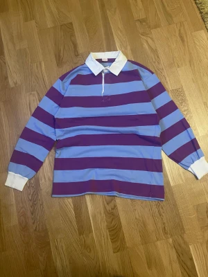 Rugby tröja lila och blå randig - Blå-lila randig Rugby tröja. Osäker på storlek eftersom att den har fadeat bort från innanför kragen men passar som en Small eller medium.