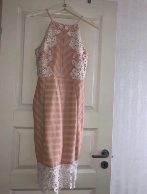 Beige spetsklänning med smala axelband - Supersnygg beige klänning från H&M med smala axelband och vita spetsdetaljer upptill och nertill. Klänningen har en figurnära passform och subtila ränder i tyget. Perfekt för dig som vill sticka ut med eleganta detaljer och modern design.