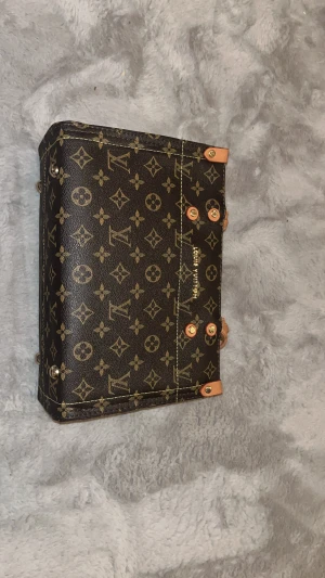 Louis Vuitton monogram axelväska - Snygg axelväska från Louis Vuitton med klassiskt monogrammönster i mörkbrunt och beige. Väskan har en boxig form, flätade handtag i ljust skinn, röd insida och guldfärgade detaljer. Medföljer justerbar axelrem och innerfack med dragkedja.