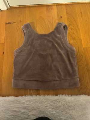 Rosa/lila croppad linnetopp i fleece - Mysig rosa/lila croppad linnetopp i mjuk fleece. Toppen är ärmlös med breda axelband och har en enkel, stilren design som passar perfekt till chill eller layering. Perfekt för dig som gillar bekväma och trendiga plagg.