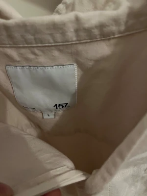 Vit skjorta från 157, storlek L - Snygg vit skjorta från 157 i storlek L. Skjortan har klassisk krage, knappar framtill och en bröstficka. Materialet känns som mjuk bomull och modellen är loose fit med korta ärmar. Perfekt för dig som gillar enkel och clean stil.