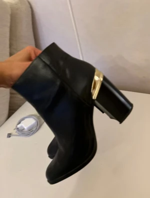 Svarta boots med gulddetalj - Snygga svarta boots i skinn med spetsig tå och hög klack. Guldfärgad detalj runt hälen ger extra edge. Perfekt till jeans eller kjol när du vill ha en stilren look med lite attityd. Strl 38