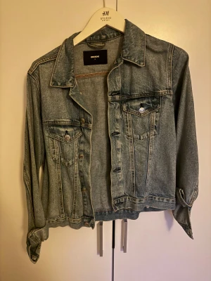 Klassisk jeansjacka från Bik Bok - Snygg ljusblå jeansjacka från Bik Bok med klassisk passform. Jackan har två bröstfickor med knappar, krage och knäppning framtill. Perfekt att slänga över en hoodie eller t-shirt för en chill look.