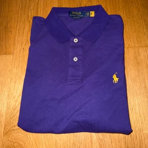 Lila piké från Ralph Lauren - Snygg lila pikétröja från Ralph Lauren, tröjan har bara testats men aldrig kommit till användning! Storlek S men sitter lite större!