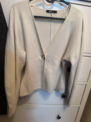 Beige kofta.  - Snygg beige kofta från Gina Tricot i storlek XS. Koftan har en djup v-ringning och stängs med en dekorativ knapp framtill. Långärmad och i mjukt stickat material som ger en chill och clean look. Perfekt att slänga på över en topp för extra stil.
