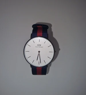 Daniel Wellington klocka - Klassisk Daniel Wellington klocka med ett quartz urverk. Armbandet är tillverkat av textil och finns ej att köpa längre. Klassisk och tidlös modell. Har fått den i gåva och använd max 3 gånger.