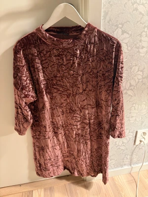 Brun sammetsklänning från Zara - Säljer en brun kort sammetsklänning från Zara med krossad effekt. Klänningen har trekvartsärm och rak passform, perfekt för dig som gillar en unik och trendig look. Materialet är mjukt och skimrande, vilket ger en cool vibe.