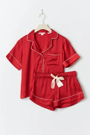 Röd silkes pyjamas  - Snygga röda pyjamasshorts i silkesliknande material med vita kontrastsömmar och en bred vit rosett framtill. Shortsen har elastisk midja och avslappnad passform, perfekta för chillkvällar hemma. Tröjan är röd med vita detaljer och röda knappar. I storlek 170 från young gina, köptes förra året.