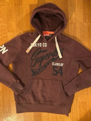 Superdry vintage hoodie JPN - En snygg vinröd vintage hoodie från superdry🤩 Bra passform och den är i riktigt bra skick! Sprucket tryck på ärmen som strålar vintage! Storlek L, passar folk över 180cm iaf, är 170cm lång på bilden. Var inte rädda att skicka prisförslag och frågor!😁✌️