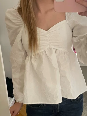 Vit blus med puffärm från Bikbok - Säljer en vit blus från Bikbok i storlek XS. Blusen har puffiga långärmar, v-ringad hals och lätt rynkade detaljer vid bysten. Subtilt mönster och struktur. 