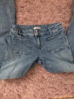 Blå jeans med stora fickor Gina Tricot - Säljer ett par blå jeans från Gina Tricot i storlek 164. Jeansen har två stora fyrkantiga fickor framtill, klassisk knappstängning och bälteshällor. Materialet är jeans och färgen är en tvättad blå nyans. Perfekt för dig som gillar en chill och trendig look.