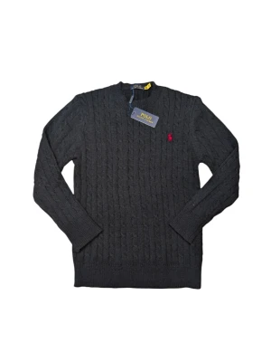 P R Lauren Svart  - Snygg mörkgrå stickad tröja från P R Lauren med klassiskt kabelmönster och röd broderad logga på bröstet. Rund hals och långa ärmar, perfekt för dig som gillar stilrena och tidlösa plagg. Materialet är mjukt och värmande ull. Passar storleken 170-180