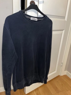 Mörkblå sweatshirt från Stone Island - Säljer en mörkblå sweatshirt från Stone Island med klassisk rund hals och ribbade muddar. Tröjan har en loose passform och är tillverkad i mjuk bomull, perfekt för chill dagar. Diskret logga i nacken och enkel design utan mönster. Tyvärr borttappad Stone Island-patch. 