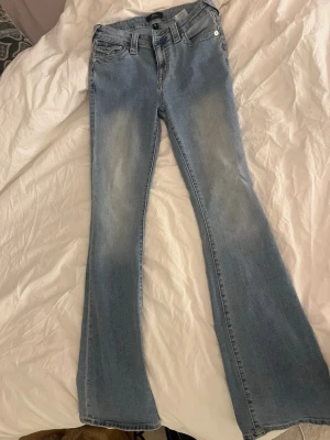 Bootcut jeans från True Religion - Snygga ljusblå bootcut jeans från True Religion med klassisk femficksdesign och tydliga sömmar. Jeansen har en ikonisk bakficka med logotyp och är tillverkade i mjukt denim-material. Perfekt för dig som gillar en avslappnad och trendig look.