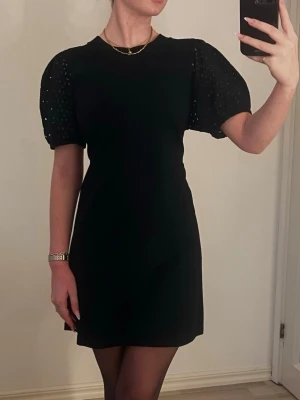 Svart kortklänning med puffärm H&M - Supersnygg svart kortklänning från H&M med puffiga kortärmar i broderad spets. Endast använd en gång. OBS!!! Jag har satt säkerhetsnålar i ryggen för definierad midja. Tycker den passar S bättre än M