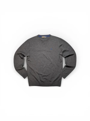 Grå stickad tröja från Morris XL - Snygg mörkgrå stickad tröja från Morris med v-ringad hals och diskret blå broderad logga på bröstet. Tröjan har långa ärmar och ribbade muddar vid hals, ärmslut och nederkant. Perfekt för dig som gillar klassisk stil med en modern touch.