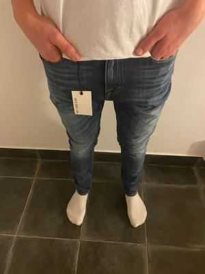 Blå jeans från tiger of sweden - Snygga blå jeans från tiger of sweden och klassisk femficksdesign. Jeansen har kontrastsömmar och en mörk tvätt med ljusa slitningar. Perfekt för dig som gillar stilrena och tidlösa jeans. Modellen är 177 cm 