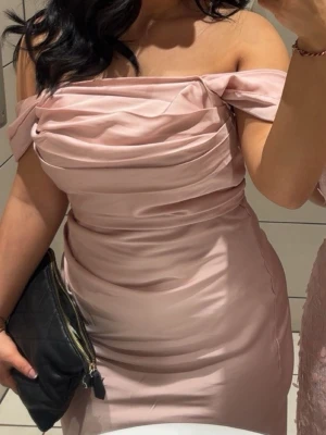 Ljusrosa  långklänning - Elegant ljusrosa långklänning i glansigt material med draperad överdel och axelbandslös design. Klänningen har figurnära passform och slät kjol som faller snyggt längs kroppen. Perfekt för speciella tillfällen när du vill sticka ut.  Axel band finns på men kan tas bort om det önskas. Banden är själv påsytt. Använd 2 gånger 