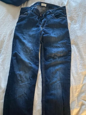 Mörkblå jeans från Lindex - Snygga mörkblå jeans från Lindex med klassisk femficksdesign och kontrastsömmar. Modellen har rak passform och normal midja, vilket gör dem enkla att matcha med olika stilar. Materialet är slitstarkt jeans och färgen är djupblå med lätt tvättad effekt.