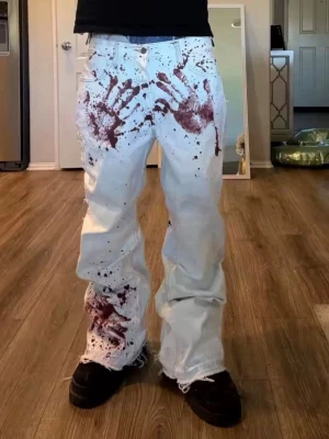 Vita wide jeans med handavtryck - Unika vita jeans med bred passform och råa, fransiga benslut. Byxorna har mörkröda handavtryck och färgstänk som ger en edgy och konstnärlig vibe. Perfekt för dig som vill sticka ut och ha något som ingen annan har. Materialet är klassisk jeans.