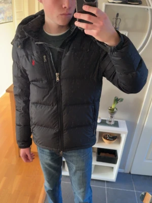 Svart pufferjacka från Polo Ralph Lauren - Svart pufferjacka från Polo Ralph Lauren med huva och dragkedja framtill. Storlek S. (182 66KG)