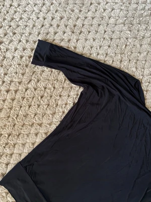 Svart omlottopp från House of Lola - Säljer en svart omlottopp från House of Lola i storlek XS. Toppen har lång ärm och bred mudd nedtill, tillverkad i mjukt och stretchigt material som känns skönt mot huden. Perfekt för dig som gillar stilrena och enkla plagg med snygg passform.