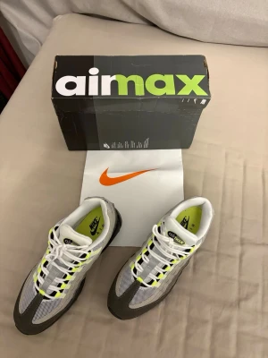Nike Air Max 95 OG Neon US10/EU44 - Nike Air Max 95 OG Neon med ikoniska detaljer i grått, vitt och neongult. Skorna har mesh och mocka i ovandelen, svart sula med synliga Air-enheter och klassisk snörning. Perfekta för dig som vill sticka ut med en retro sneakerklassiker.