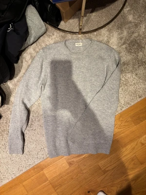 Grå stickad tröja från John Henric - Snygg grå stickad tröja från John Henric med rund hals och ribbade muddar vid ärmslut och nederkant. Tröjan har en klassisk passform och är perfekt för lager-på-lager under kyliga dagar. Enkel och stilren design som funkar till jeans eller chinos.
