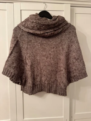 Stickad poncho - Stickad poncho med stor krage. Märket är Promod men det står ingen storlek men jag skulle säga S o M. Färgen är lite brun aktig som man kan se på bilden😇
