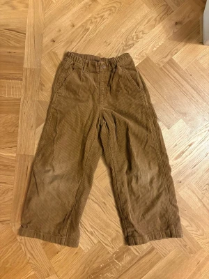 Bruna manchesterbyxor med bred passform - Säljer ett par bruna manchesterbyxor med bred passform och klassiska fickor fram. Byxorna har knäppning i midjan och är tillverkade i mjukt manchestertyg som ger en skön retrovibe. Storlek 7-8 år från UniQlo