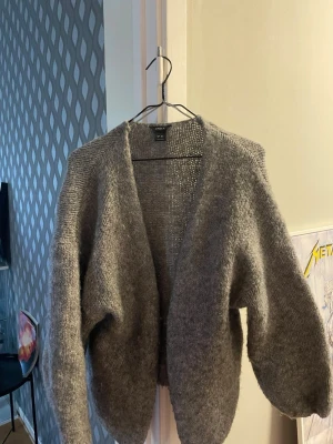 Grå stickad kofta från Index - Mysig grå stickad kofta från Index med loose passform och långärmade ärmar. Koftan har en öppen front utan knappar eller dragkedja, perfekt att slänga på sig när det är kyligt. Passar dig som gillar enkel och avslappnad stil.