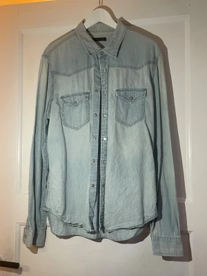 Ljusblå jeansskjorta Calvin Klein Jeans XL - Säljer en ljusblå jeansskjorta från Calvin Klein Jeans i storlek XL. Skjortan har klassisk krage, två bröstfickor med knappar och tryckknappar längs hela framsidan. Materialet är mjuk bomull och passformen är normal. Perfekt för dig som gillar stilren denim.