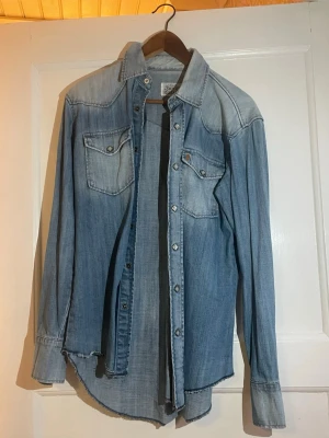 Silver Dollar jeansskjorta i ljusblå denim - Snygg ljusblå jeans skjorta från Silver Dollar med klassisk westernstil. skjortan har två bröstfickor med knappar, långa ärmar och en rak passform.