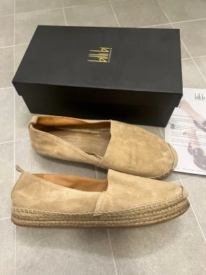 Beige espadrillos från Billi Bi - Säljer ett par snygga beige espadrillos från Billi Bi Copenhagen. Skorna har ovandel i mjuk mocka och en klassisk flätad sula i jute. De har rund tå och är fodrade med skinn på insidan för extra komfort. Perfekta för varma dagar och enkel stil.
