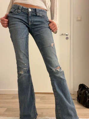 Blå bootcut jeans med broderi - Säljer ett par blå bootcut jeans med slitningar på knäna och snygga broderade bakfickor med silverdetaljer och paljetter. Jeansen har låg midja och klassisk femficksmodell. Materialet är jeans i bomull med lite stretch för skön passform. Passar på någon som är 170cm och kortare 🫶🏻