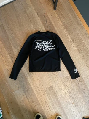 Svart långärmad tröja  - Svart långärmad topp med vit broderad text 'Never Forget' på ryggen och ärmen. Streetstyle