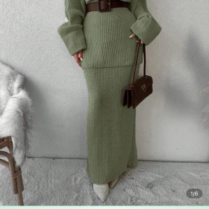 Olivgrön stickad långärmad tröja med matchande kjol - Snygg och mysig höst-/vinterlook med olivgrön stickad tröja och olivgrön stickad långkjol. Tröjan har rund hals, lång ärm och en loose passform med grovstickad struktur som ger en avslappnad, chill vibe. Kjolen har rak passform, bred resår i midjan och ribbstickning med mjuk, chunky känsla – perfekt för kalla dagar. Tillsammans skapar de en harmonisk, trendig outfit som är enkel att styla med boots eller sneakers för både vardag och lite uppklädda tillfällen.