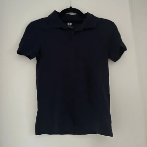 Mörkblå piké t-shirt från H&M - Snygg mörkblå piké t-shirt från H&M Basic, tillverkad i ekologisk bomull. Klassisk krage och korta ärmar ger en clean och stilren look. 