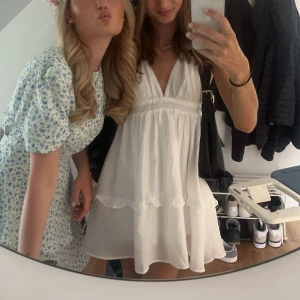 Vit kort klänning med öppen rygg - Supersöt vit kort klänning med v-ringning och volangdetaljer. Klänningen har öppen rygg med knytband och är ärmlös. Perfekt för sommarens alla tillfällen och ger en riktigt fräsch och luftig känsla