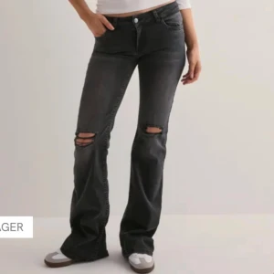 Svarta bootcut jeans med slitningar - Snygga svarta jeans med bootcut passform och slitna hål över knäna. Jeansen har klassisk femficksdesign, knapp och dragkedja framtill. Perfekta för dig som gillar en edgy och avslappnad stil. Jeansen är aldrig använda och är helt nya men prislappen är inte kvar.