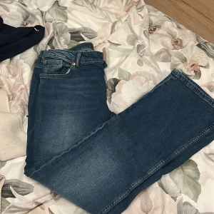 Blå bootcut jeans i klassisk modell - Säljer ett par blå jeans med bootcut passform och klassisk femficksdesign. Jeansen har en snygg tvättad look och raka ben som blir vidare nedtill. Perfekta för dig som gillar en retrostil och vill ha ett par jeans som sticker ut lite extra.