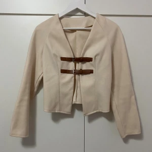 Beige tröja med bältesdetaljer - Stilren beige tröja med två bruna bältesdetaljer framtill. Perfekt för dig som gillar minimalistisk och clean stil✨ Aldrig använt, storlek S, nypris 209kr! Pris kan diskuteras 🤗