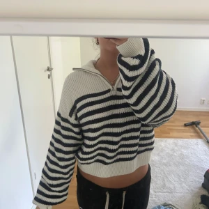 Randig stickad half zip tröja - Säljer en stickad tröja med marinblå och vita ränder. Tröjan har en half zip-dragkedja och krage, samt långa ärmar och loose passform. Perfekt för dig som gillar en chill och trendig stil.