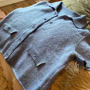 Blå stickad kofta med kort ärm - Superfin blå stickad kofta från hm med korta ärmar, krage och knappar hela vägen fram. Två fickor framtill med ribbade detaljer och knappar. 