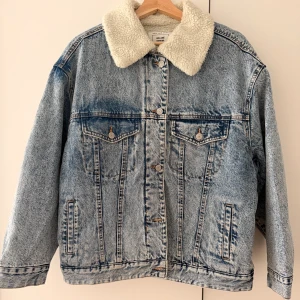Jeansjacka med teddykrage Pull&Bear - Snygg blå jeansjacka från Pull&Bear med vit teddykrage. Klassisk modell med knappar framtill, två bröstfickor och två sidofickor. Jackan har en oversized känsla och är perfekt för lager-på-lager-stil under höst och vinter.