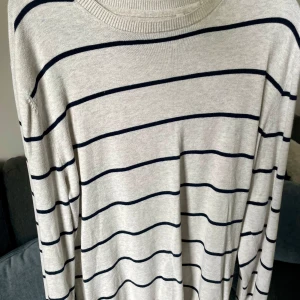 Randig beige tröja  - Snygg beige långärmad tröja från Canda med mörkblå horisontella ränder. Tröjan har rund hals och är gjord i mjukt bomullsmaterial som känns skönt mot huden. Perfekt för dig som gillar enkel och stilren design. Funkar som unisex/oversized